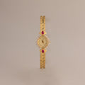 The Art Deco Ruby Timepiece features a gold bracelet and gemstone accents on the face, evoking retro glamour, shown against a plain beige background.