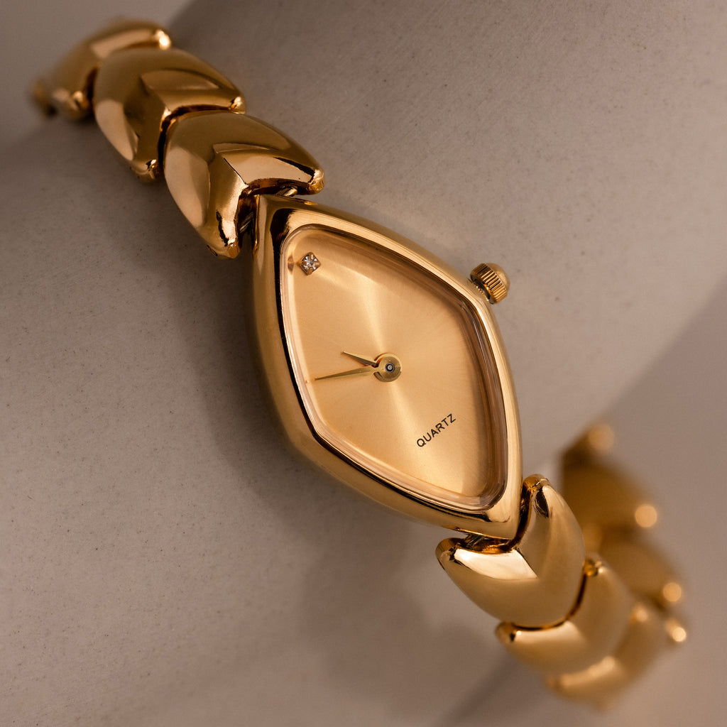 Macro shot of the gold oval watch dial with a single crystal at the 12 o’clock mark, revealing the fine brush texture and minimalist quartz face