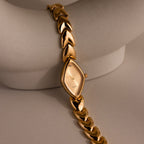 Geometric Oval Timepiece wristwatch with an oval-shaped dial and leaf-link band, displayed on a curved, light-colored surface.