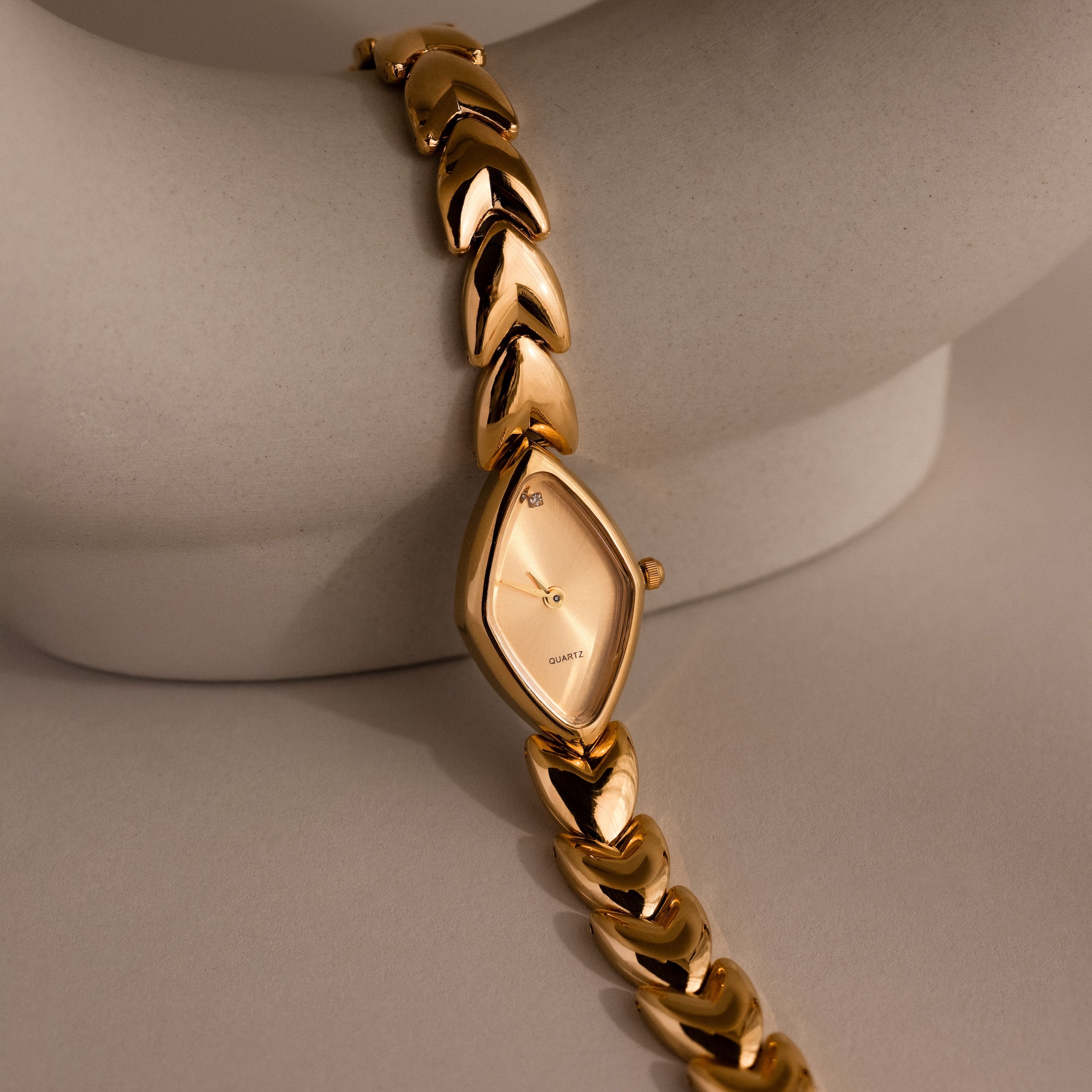 Geometric Oval Timepiece wristwatch with an oval-shaped dial and leaf-link band, displayed on a curved, light-colored surface.