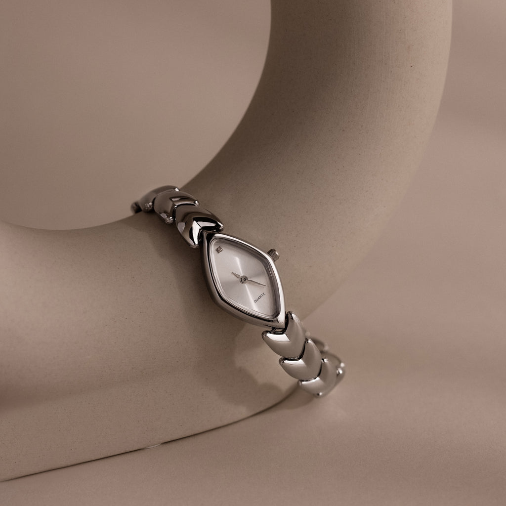 Studio shot of a silver geometric wristwatch elegantly wrapped around a minimalist curved ceramic display, highlighting the unique silhouette of the timepiece.