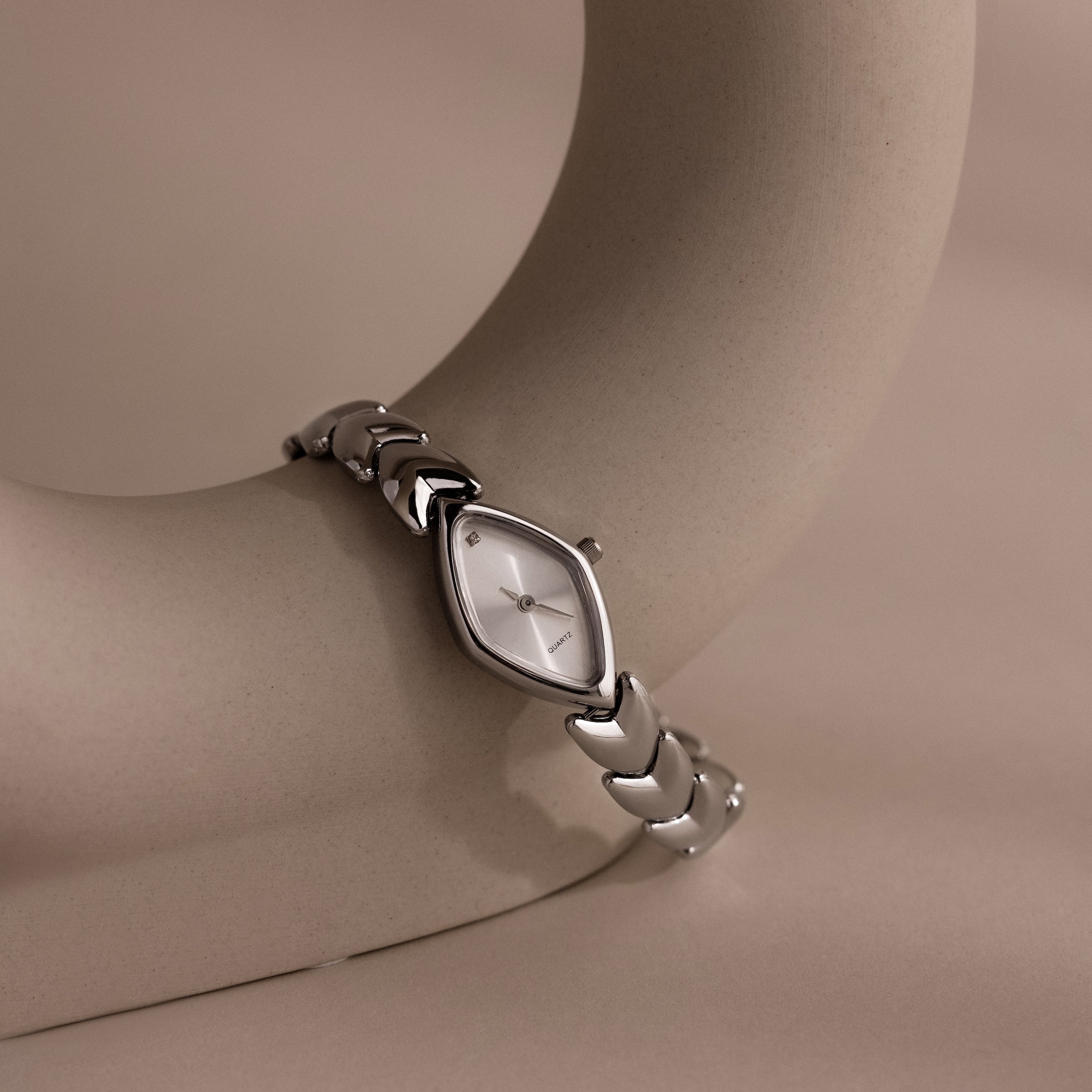 Studio shot of a silver geometric wristwatch elegantly wrapped around a minimalist curved ceramic display, highlighting the unique silhouette of the timepiece.