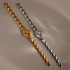 Gold and silver geometric oval watches with chevron-link bands on a neutral background.