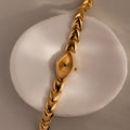 Top-down product shot of the watch laid across a ceramic ring, emphasizing the geometric marquise-shaped face and gold chevron links.