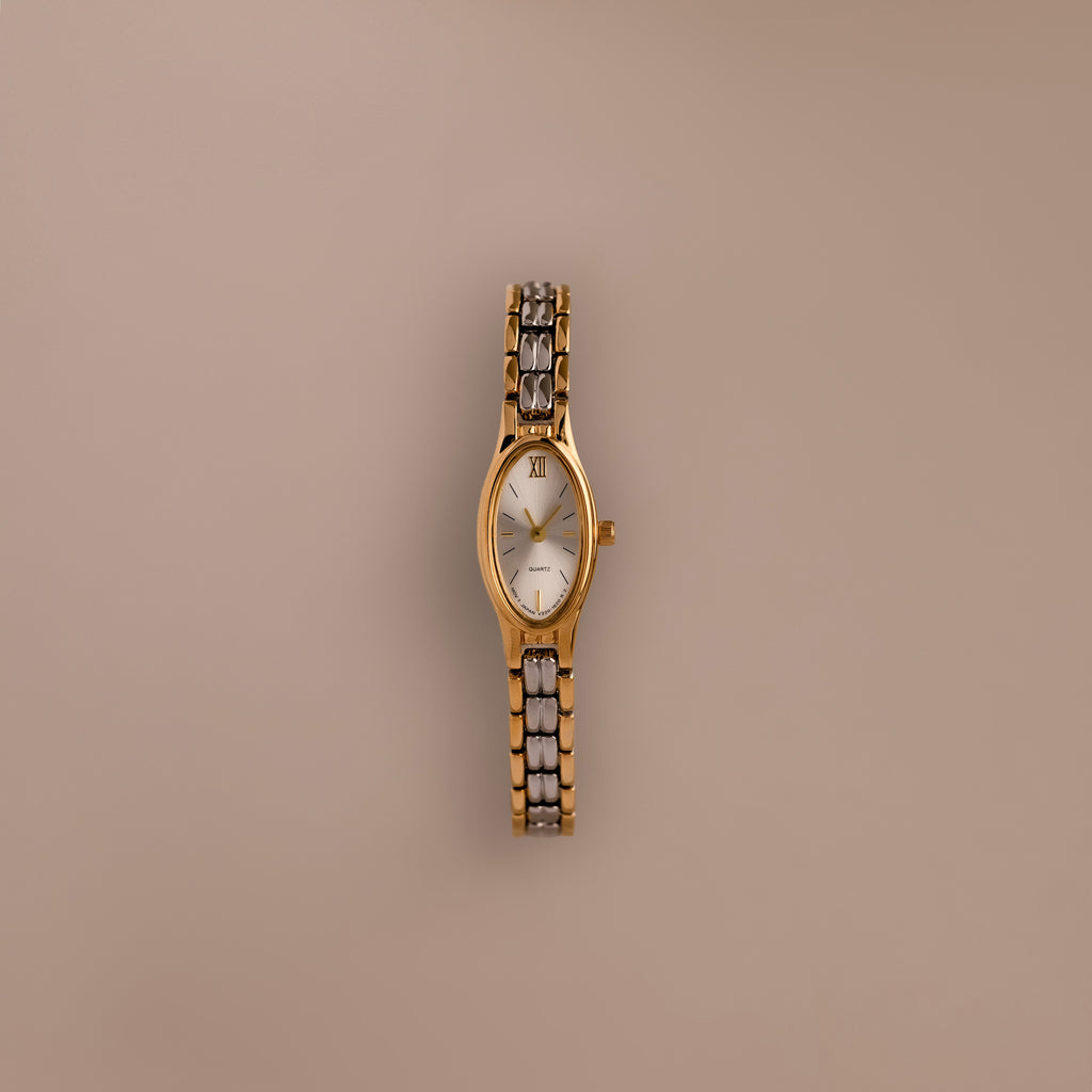 Slim Oval Timepiece in Mixed Metal, featuring a polished gold and silver link bracelet, displayed against a plain beige background.