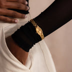 A person wearing the Slim Oval Timepiece in 18K Gold and cream pants, with one hand in their pocket.