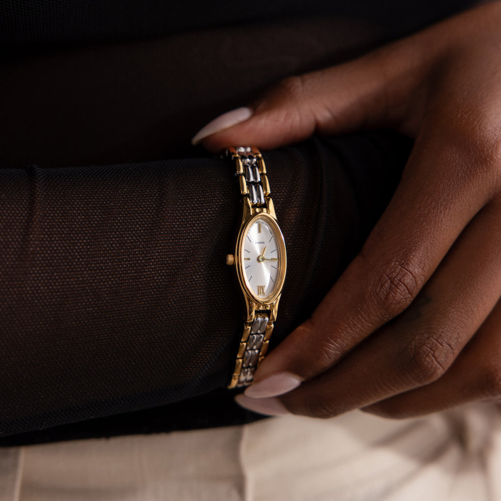 Close-up of a person wearing the Slim Oval Timepiece in Mixed Metal, featuring a white face, Roman numerals, and a polished link bracelet.