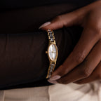 Close-up of a person wearing the Slim Oval Timepiece in Mixed Metal, featuring a white face, Roman numerals, and a polished link bracelet.