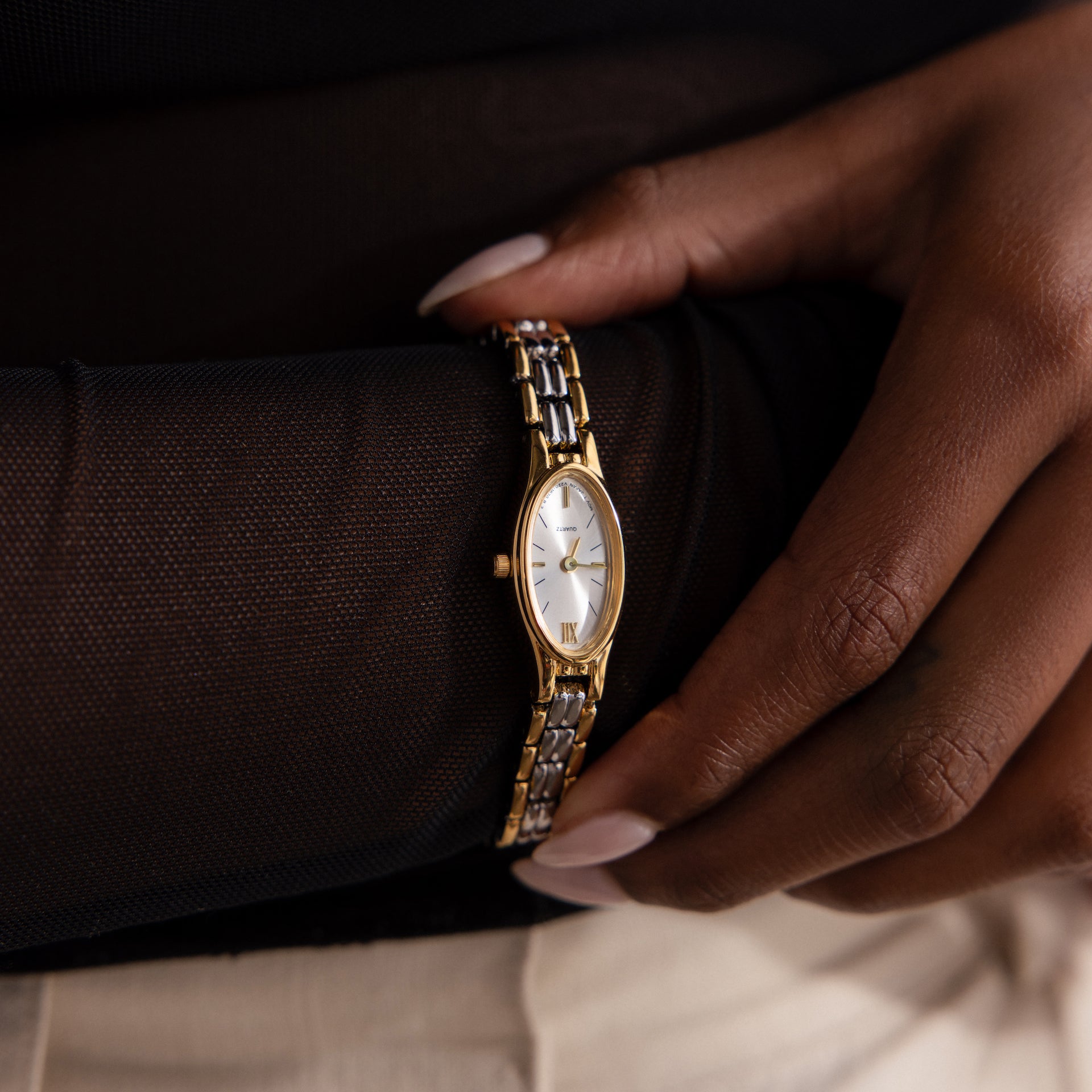 Close-up of a person wearing the Slim Oval Timepiece in Mixed Metal, featuring a white face, Roman numerals, and a polished link bracelet.