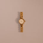 The Heart Link Timepiece is a gold wristwatch featuring heart-shaped links and a minimalist dial, displayed on a light beige background.