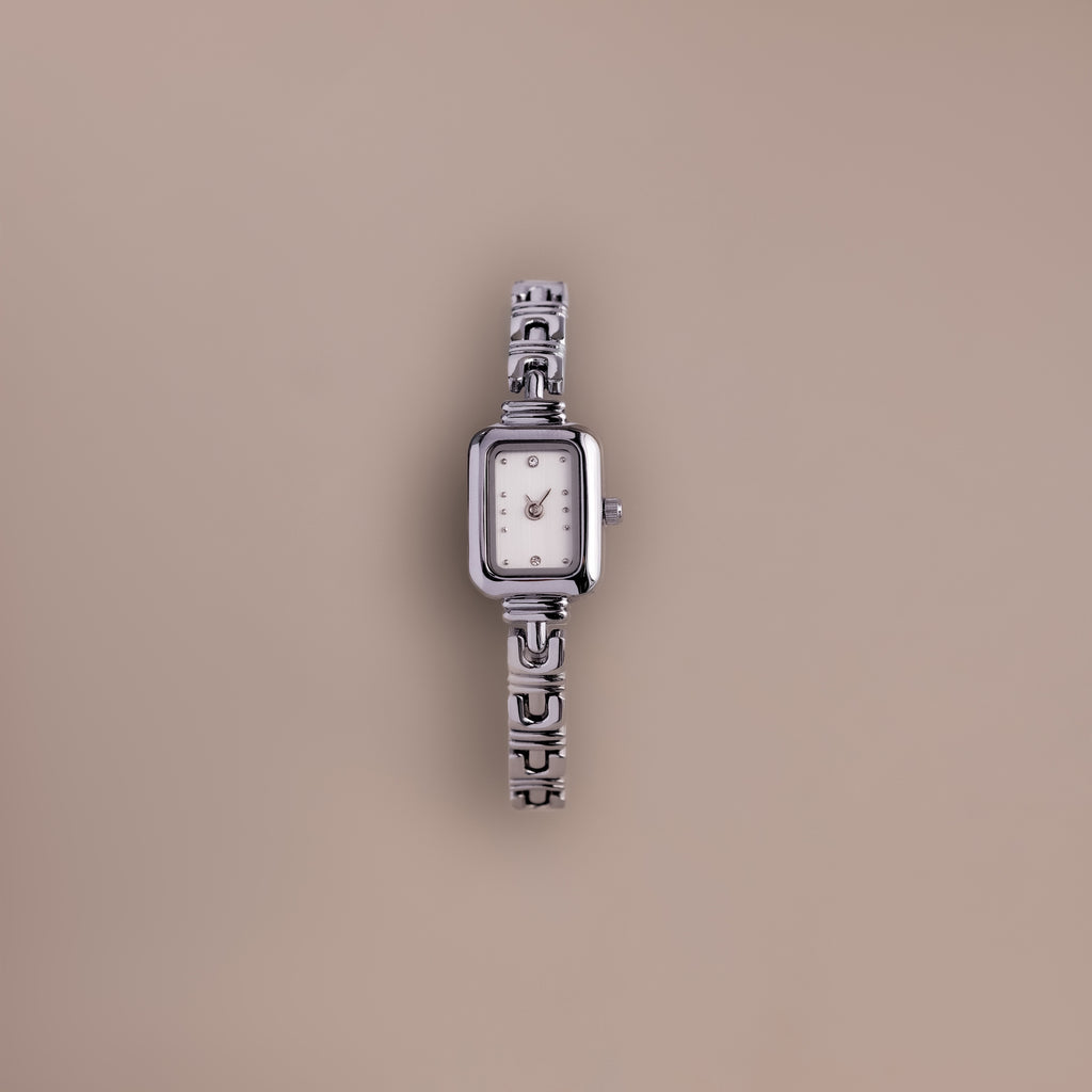 An Azteca Link Timepiece in White Gold with a patterned interlocking bracelet and rectangular white face is displayed against a plain beige background.