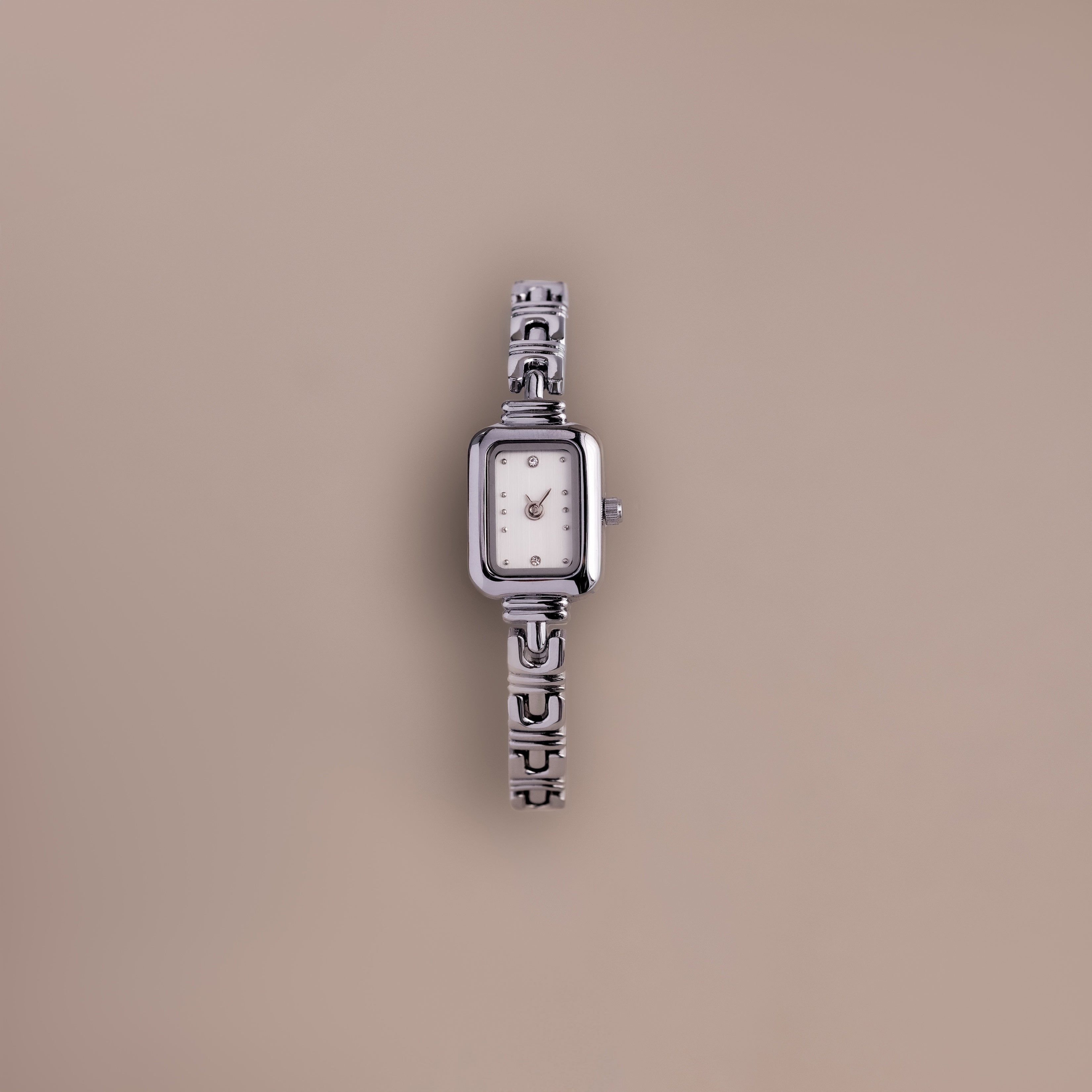An Azteca Link Timepiece in White Gold with a patterned interlocking bracelet and rectangular white face is displayed against a plain beige background.