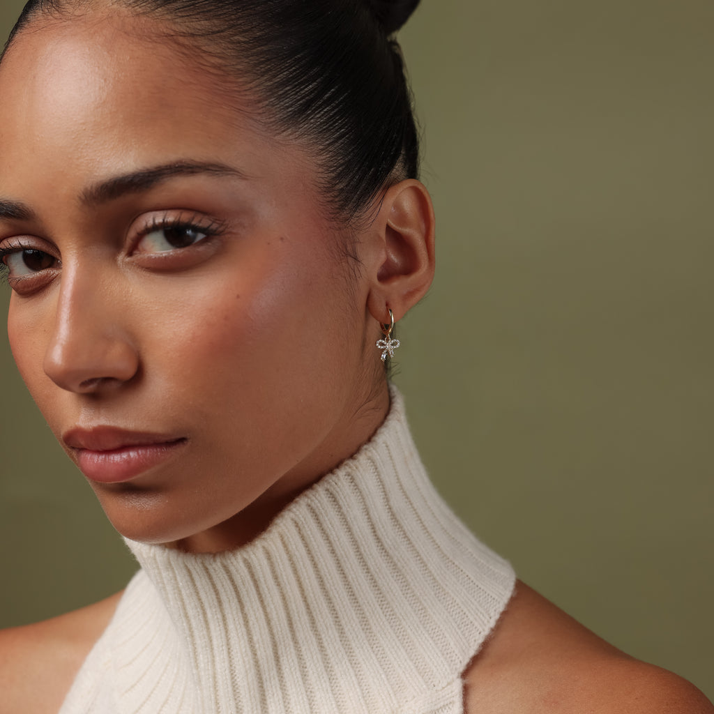 Model wearing our Pave Bow Charm Hoops against a green background