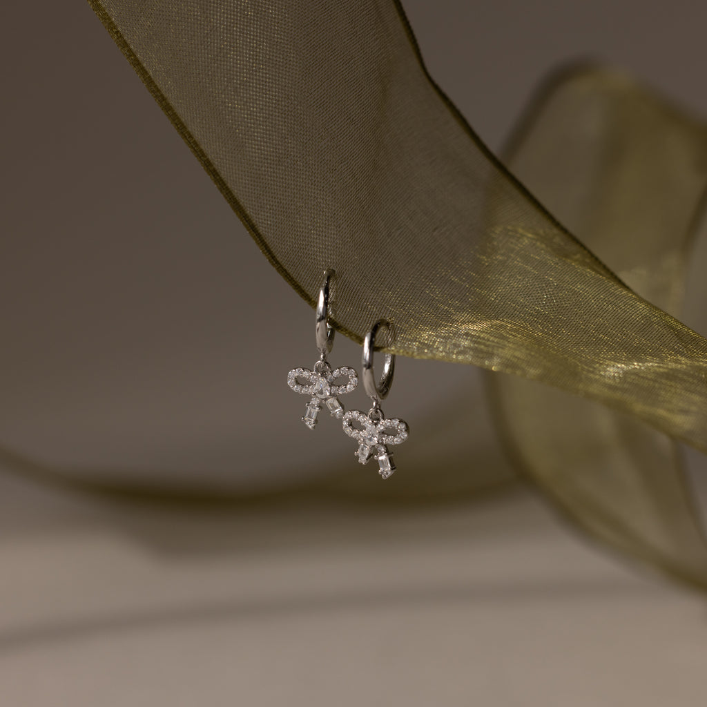 Flatlay of our Pave Bow Charm Hoops
 in Silver on a green ribbon