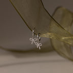 Flatlay of our Pave Bow Charm Hoops
 in Silver on a green ribbon