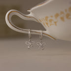 Pave Bow Charm Hoops earrings in Silver hanging from a teacup with floral patterns.