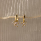 Gold diamond bow hoop earrings on a beige fabric background