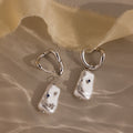 Starry Baroque Pearl Charm Hoops in White Gold, featuring blue gem accents, rest on a soft beige fabric background, bringing an elegant touch to these unique asymmetrical pearl earrings.