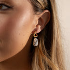 Close-up of a woman's ear wearing the Starry Baroque Pearl Charm Hoops in 18K Gold, featuring a dangling, irregular Baroque pearl.