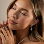 Woman with closed eyes smiles softly, hands together, wearing Starry Baroque Pearl Charm Hoops in 18K Gold and a white halter top.