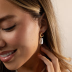 A woman smiles, wearing Starry Baroque Pearl Charm Hoops in 18K Gold, with her hand gently touching her ear.