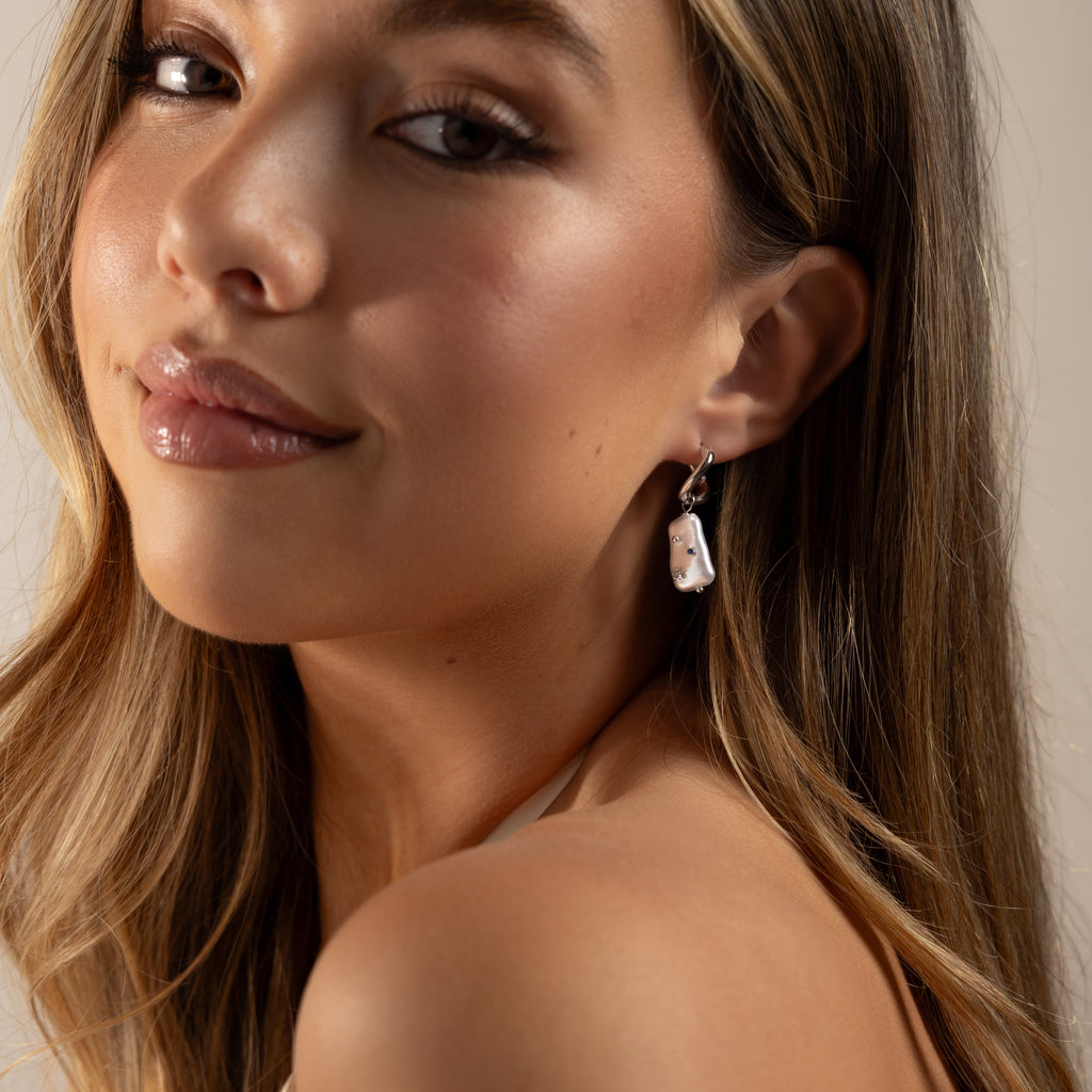 Young woman with long hair and glossy lips wears Starry Baroque Pearl Charm Hoops, glancing over her shoulder.