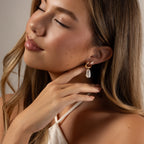 A woman with long hair gently touches her Pearl Diamond Cluster Studs and smiles softly with her eyes closed.