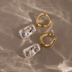 The Starry Baroque Pearl Charm Hoops in 18K Gold feature irregular pearls, blue stones, and gold accents that shine elegantly on a sunlit surface.