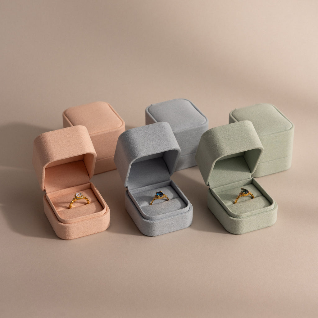 Three gold rings in Suede Ring Boxes—pink, gray, and green—arranged on a neutral background for a minimalist touch.