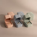 Three gold rings in Suede Ring Boxes—pink, gray, and green—arranged on a neutral background for a minimalist touch.
