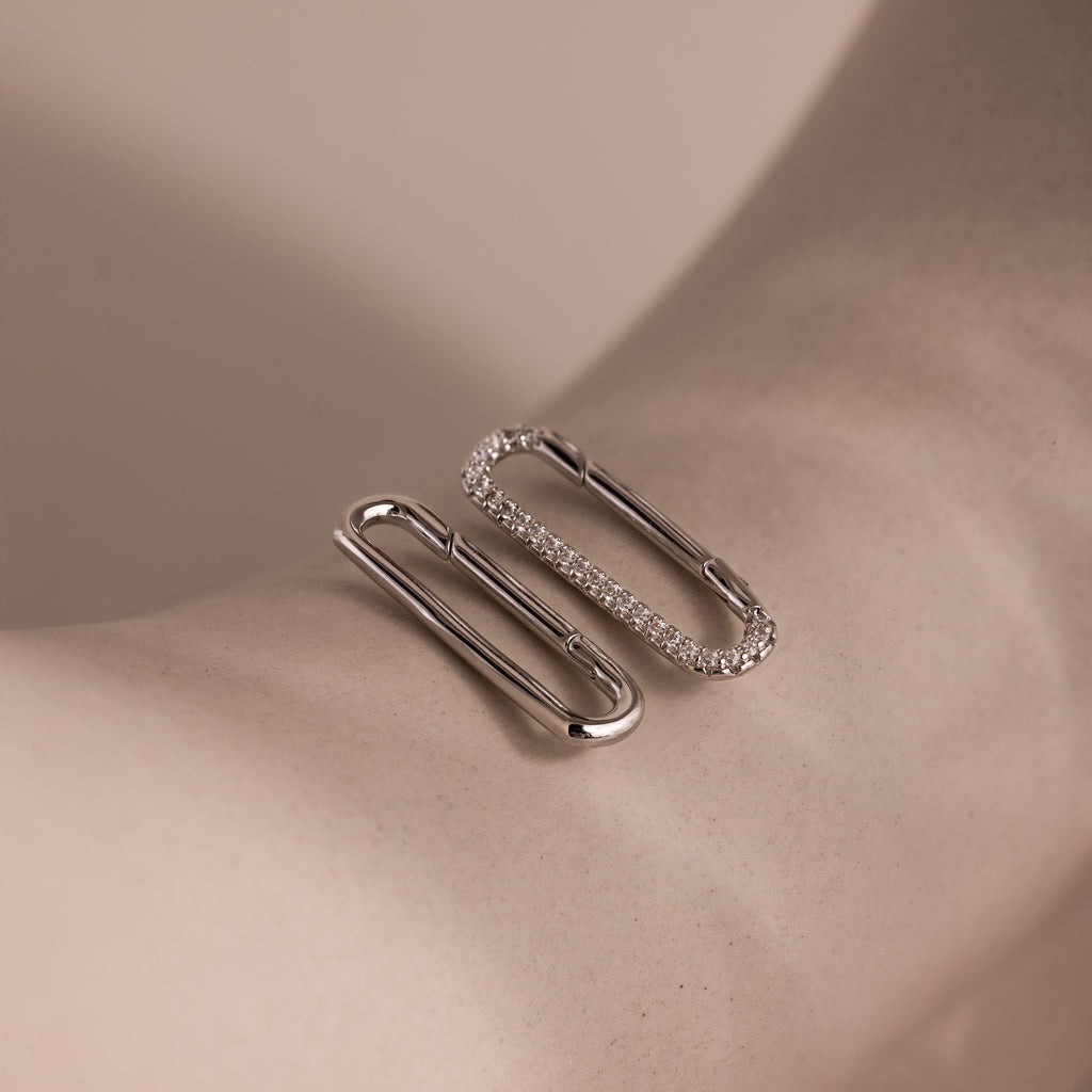 The Multipurpose Pave Link Clasp Set in White Gold features two elegant, paperclip-shaped bracelets with sparkling gemstones, shown on a light beige surface—ideal for versatile jewelry styling.