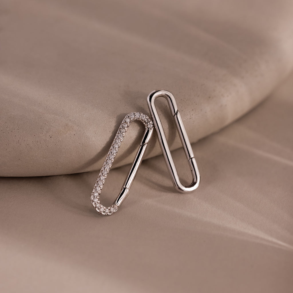 Two silver oval earrings, one with small crystals, rest on a beige surface—perfect for jewelry styling or pairing with the elegant Multipurpose Pave Link Clasp Set in White Gold.