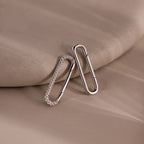 Two silver oval earrings, one with small crystals, rest on a beige surface—perfect for jewelry styling or pairing with the elegant Multipurpose Pave Link Clasp Set in White Gold.