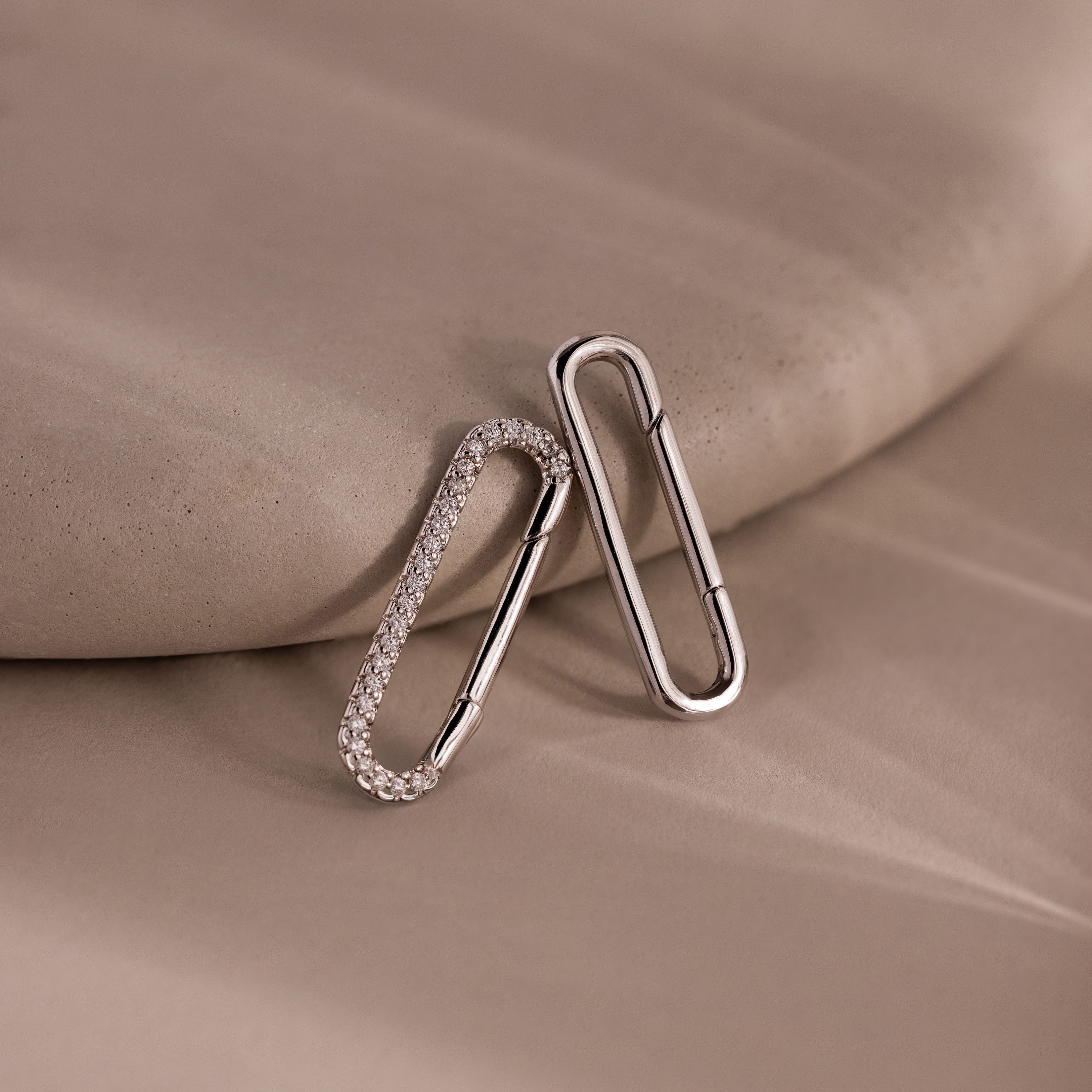 Two silver oval earrings, one with small crystals, rest on a beige surface—perfect for jewelry styling or pairing with the elegant Multipurpose Pave Link Clasp Set in White Gold.