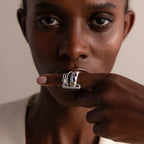 A woman gazes ahead, her hand adorned with silver rings and a Multipurpose Pave Link Clasp Set in White Gold at her lips, elegantly showcasing refined jewelry style.