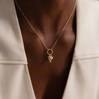 The Hummingbird Charm in 18K Gold features a diamond accent, shown layered over a cream blazer on medium-dark skin—a refined and meaningful gift choice.