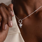 Wearing the Hummingbird Charm in Sterling Silver, someone holds the pendant near their collarbone—a beautiful and meaningful gift.