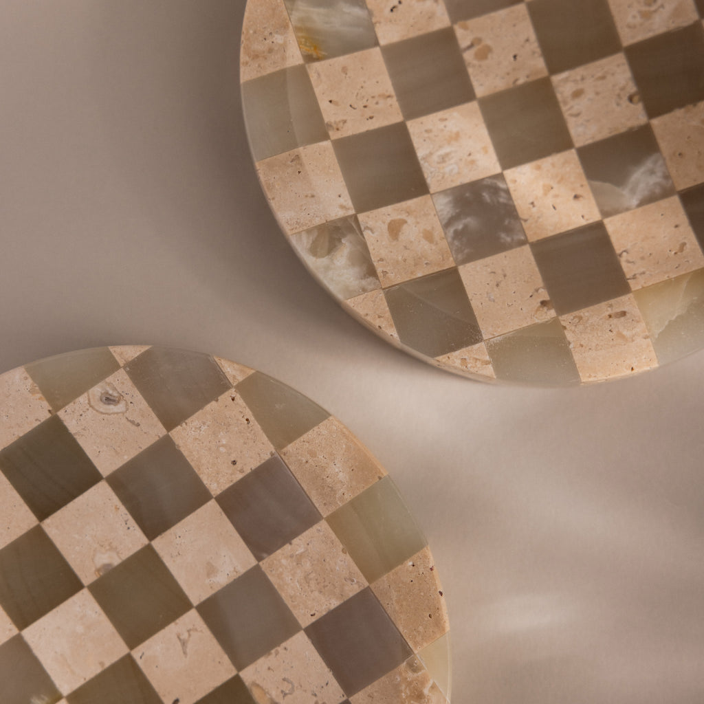 Two round, beige and taupe natural stone dishes with a checkerboard pattern are partially shown on a neutral background—ideal as the Checkered Jewelry Dish to hold your favorite pieces.