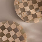Two round, beige and taupe natural stone dishes with a checkerboard pattern are partially shown on a neutral background—ideal as the Checkered Jewelry Dish to hold your favorite pieces.