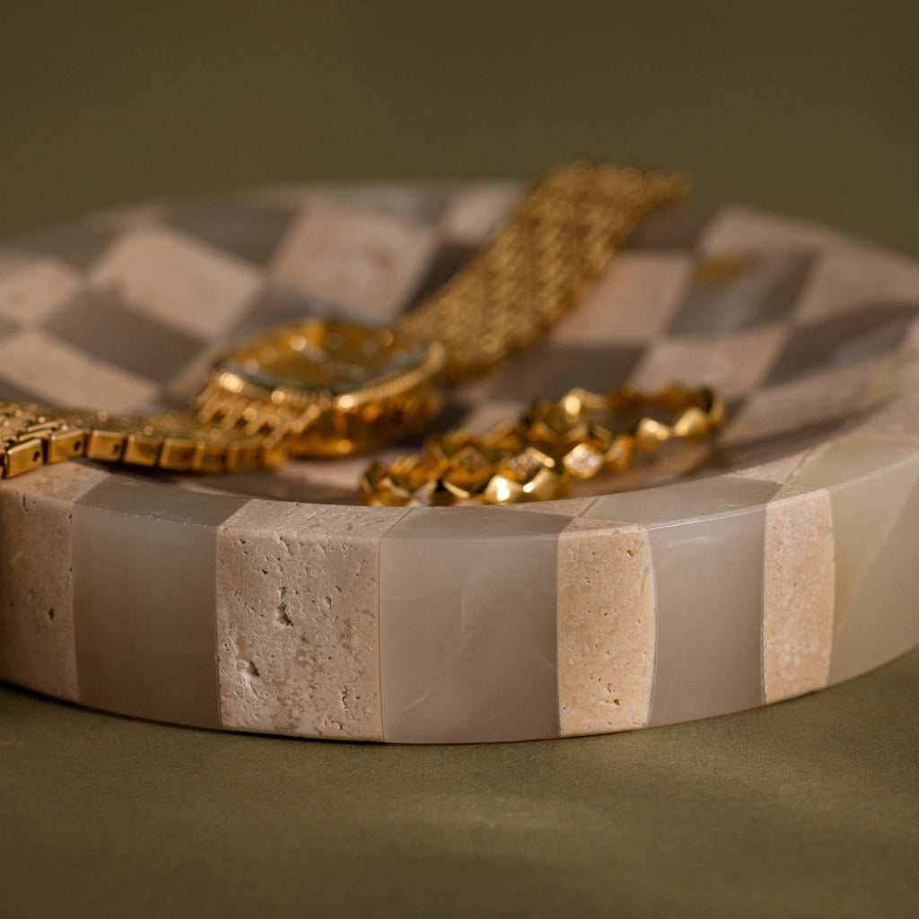 Checkered Jewelry Dish displaying a gold watch and bracelet on its round surface with beige and tan striped patterns.