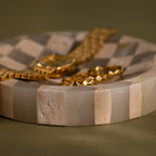 Checkered Jewelry Dish displaying a gold watch and bracelet on its round surface with beige and tan striped patterns.