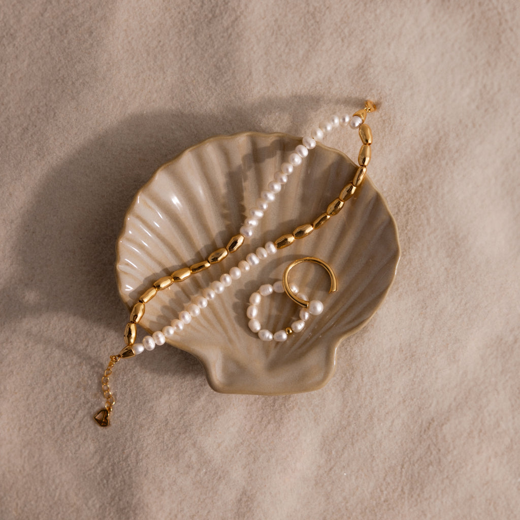 Gold and pearl jewelry displayed on the Venus Shell Jewelry Dish, resting on beige fabric for an elegant coastal decor accent.