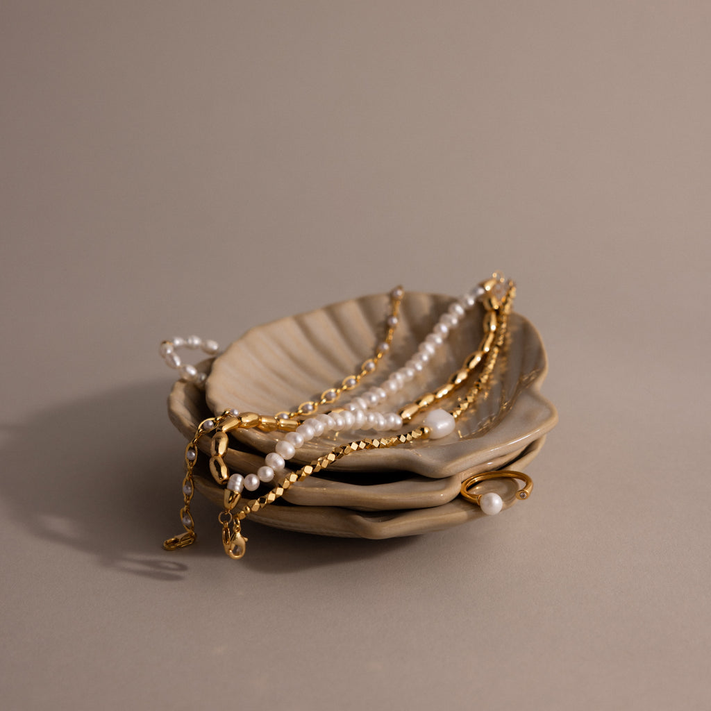 The Venus Shell Jewelry Dish holds gold and pearl jewelry on a neutral background—an elegant ceramic holder that’s perfect for coastal decor.