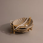 The Venus Shell Jewelry Dish holds gold and pearl jewelry on a neutral background—an elegant ceramic holder that’s perfect for coastal decor.