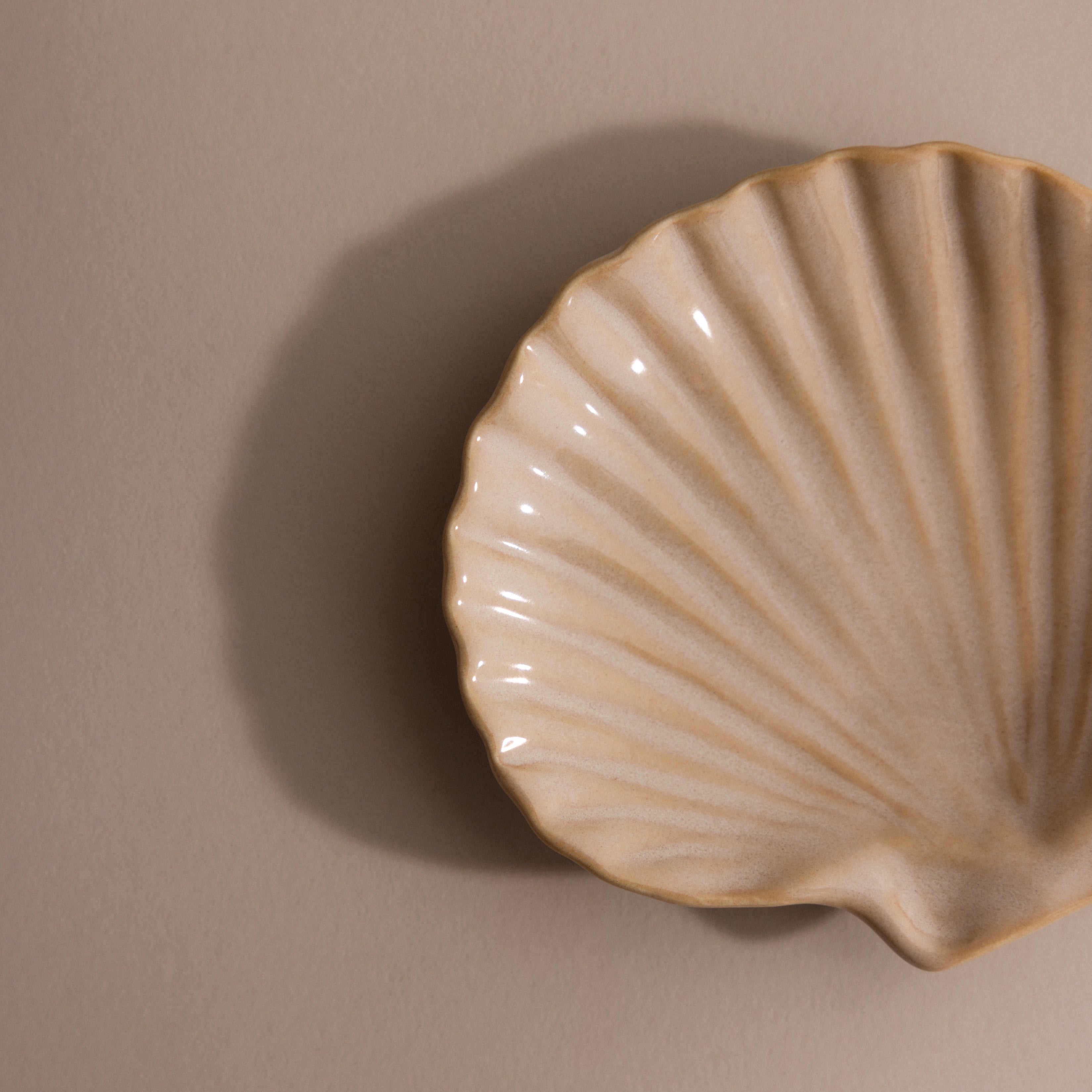The Venus Shell Jewelry Dish is a beige ceramic scallop shell, ideal as a jewelry holder or accent piece for coastal decor, displayed on a neutral background.