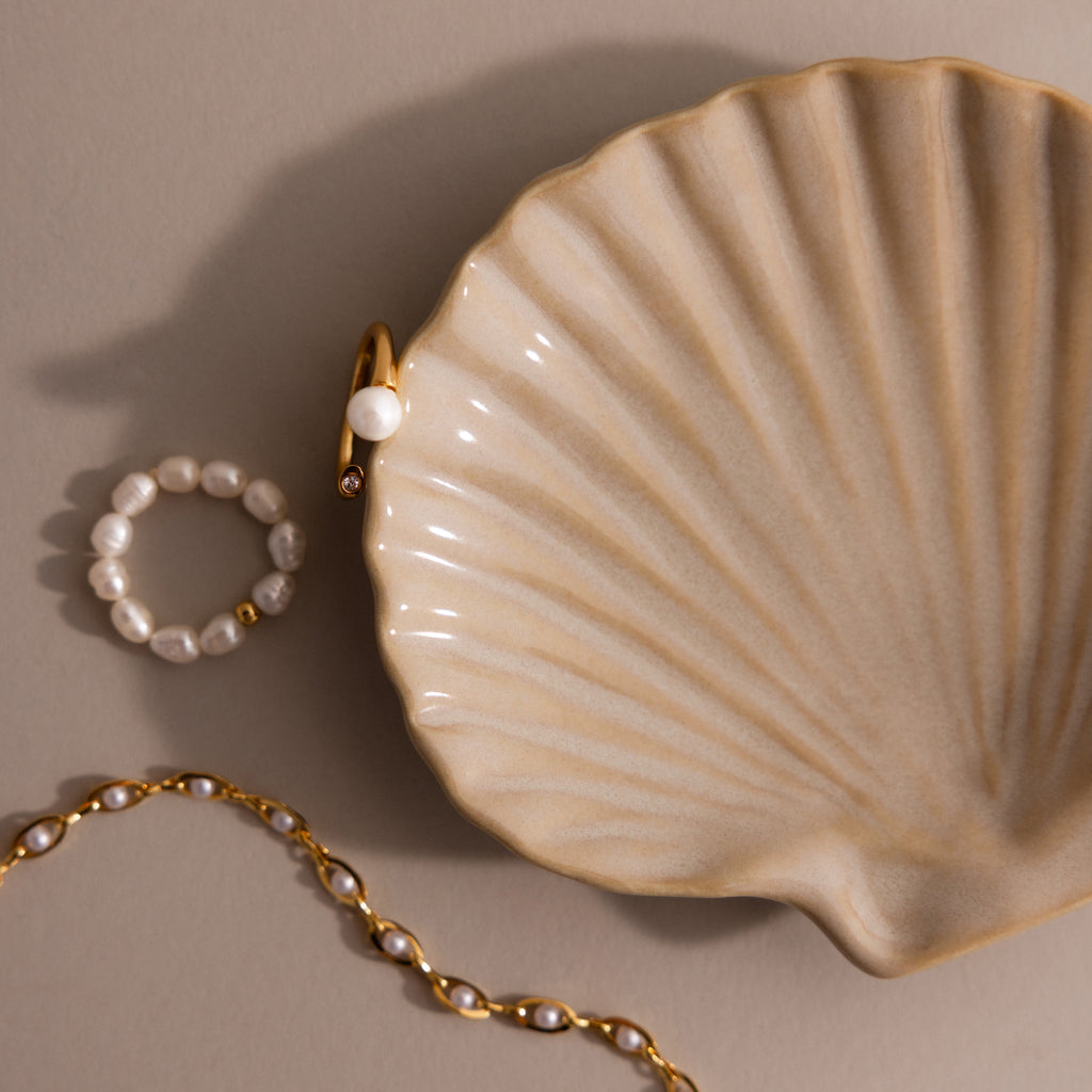 Gold and pearl jewelry rest beside the Venus Shell Jewelry Dish, creating an elegant coastal décor accent against a neutral backdrop.