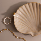 Gold and pearl jewelry rest beside the Venus Shell Jewelry Dish, creating an elegant coastal décor accent against a neutral backdrop.