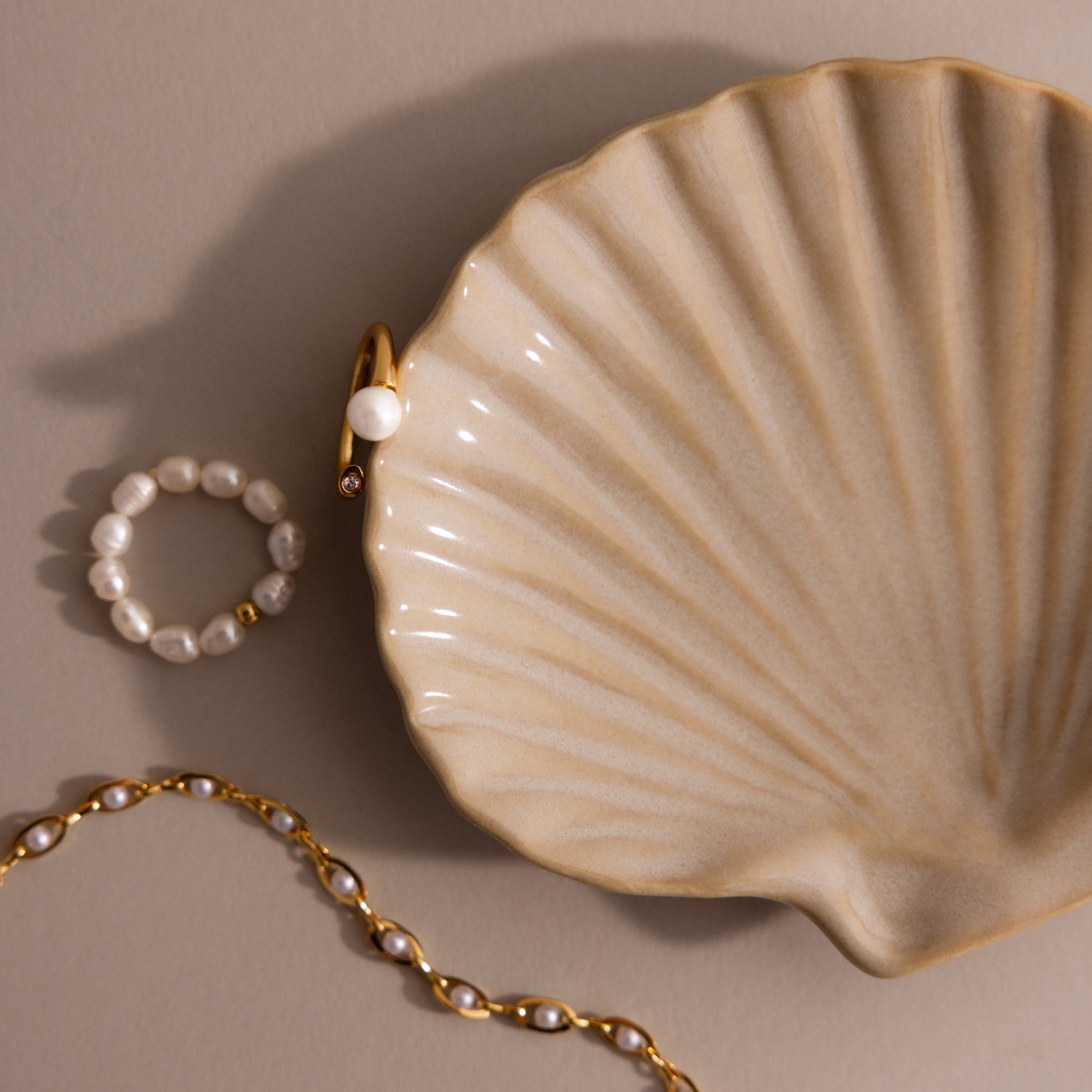 Gold and pearl jewelry rest beside the Venus Shell Jewelry Dish, creating an elegant coastal décor accent against a neutral backdrop.