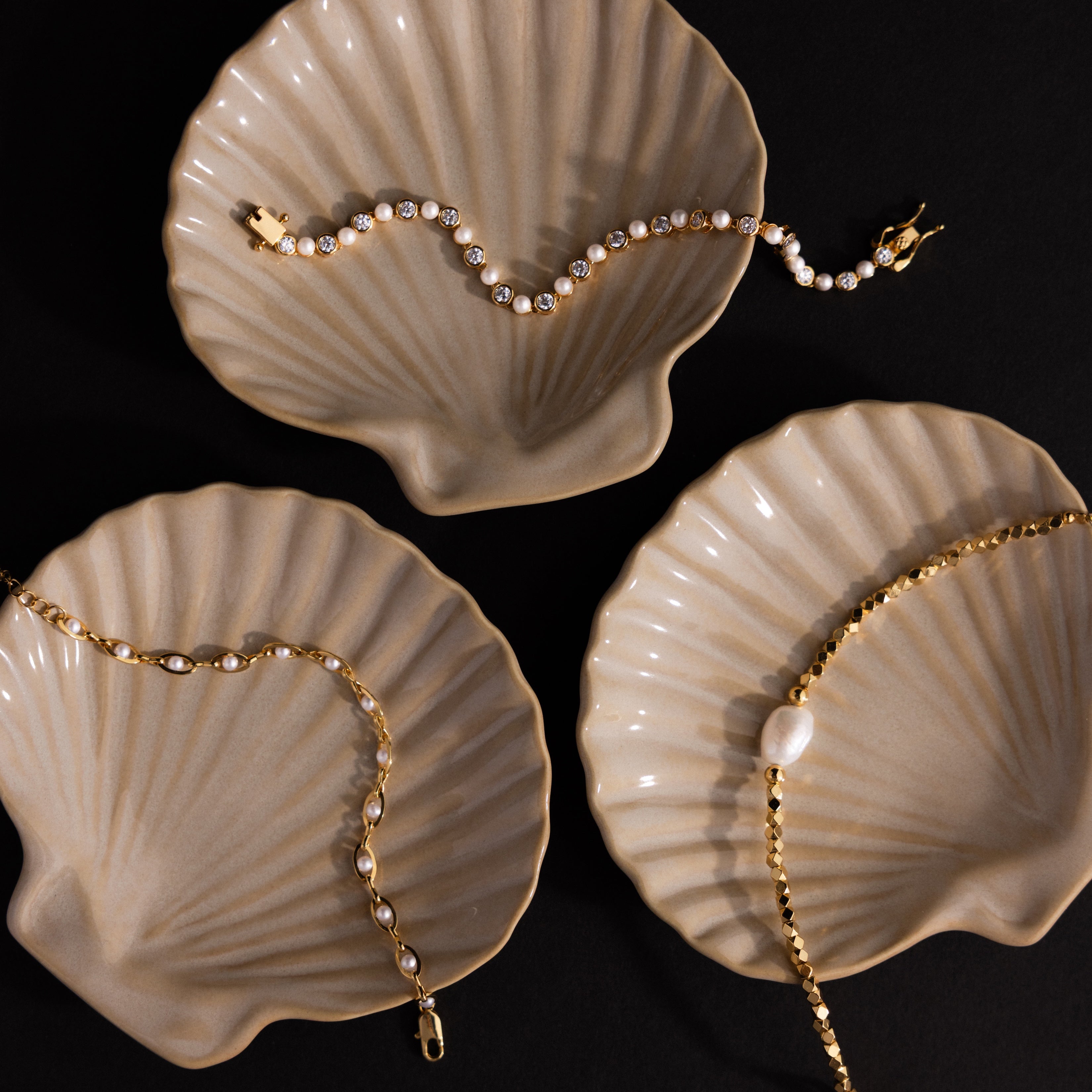 Three gold bracelets rest on beige Venus Shell Jewelry Dishes, highlighting the elegant design of the Venus Shell Jewelry Dish against a black background for a coastal decor accent.