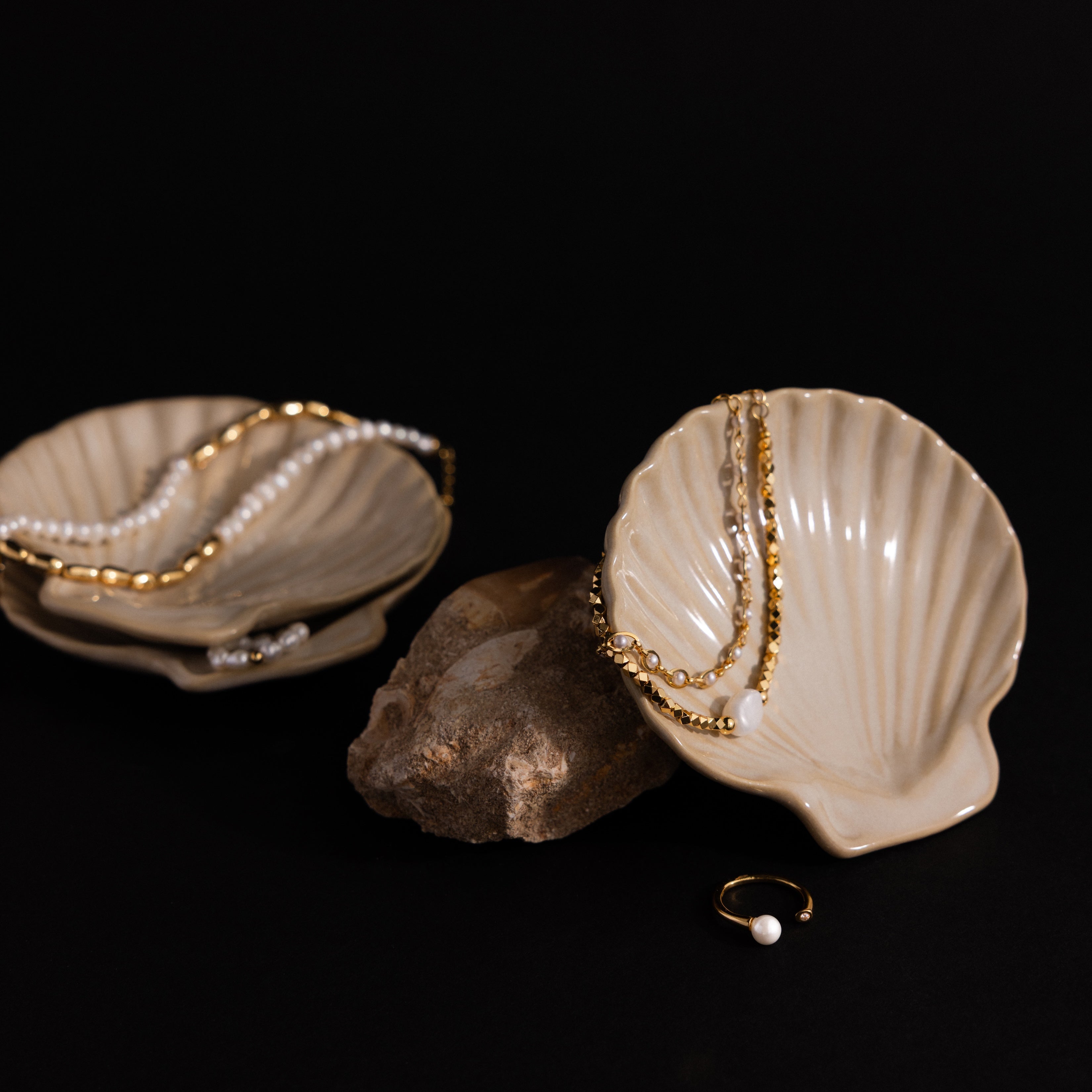 Gold and pearl jewelry rest on the Venus Shell Jewelry Dish and stone, creating stunning coastal decor with a sleek black background.